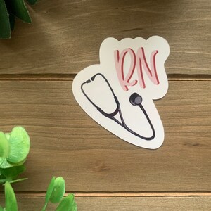 May include: A white sticker with a black stethoscope and the word "RN" in pink lettering.