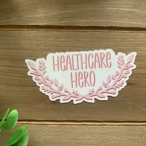 May include: Pink sticker with a floral wreath design and the text "Healthcare Hero".