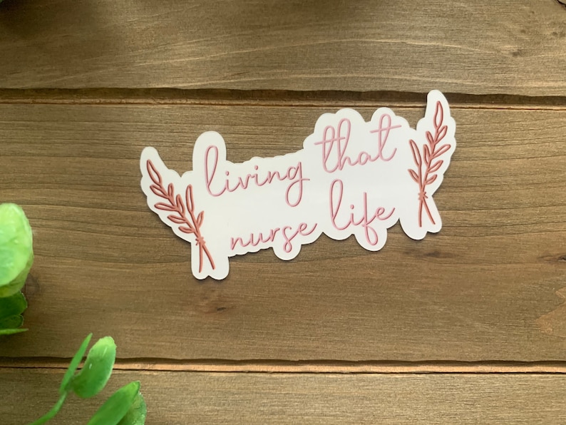 May include: White sticker with pink text that reads "living that nurse life" with two brown leafy sprigs on either side.