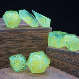 May include: A set of green and yellow dice with gold numbers. The dice are made of a translucent material and have a speckled appearance. The dice are arranged on a wooden surface.