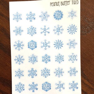 May include: A sheet of 31 blue snowflake stickers with white numbers 1 through 31. The sheet is labeled "Peanut Butter Taco".