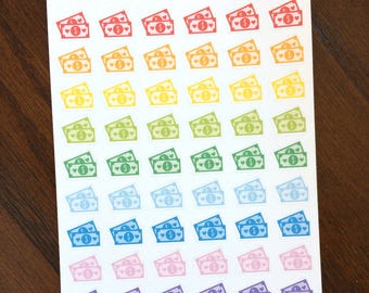 May include: A sheet of stickers with a repeating design of colourful dollar bills, each with a heart symbol. The stickers are in a range of colours, from red to black, with the text "Peanut Butter Taco" at the top of the sheet.