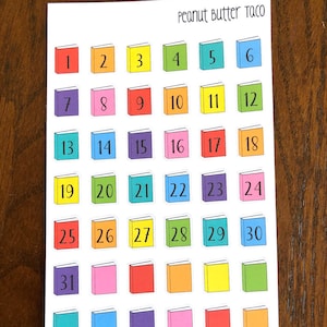 May include: A sheet of colourful book-shaped stickers with numbers 1 to 31. The stickers are arranged in rows and columns. The text "Peanut Butter Taco" is at the top of the sheet.