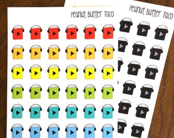 May include: A sheet of colourful stickers featuring a book with headphones and a play button. The stickers are arranged in rows of six, with each row featuring a different colour. The text "Peanut Butter Taco" is printed at the top of the sheet.