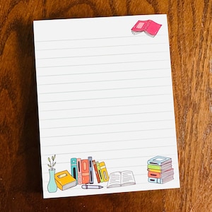 May include: A white lined notepad with a book illustration in the top right corner. The bottom of the notepad features a stack of books, a single book, a vase with a plant, and a pen.