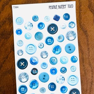 May include: A sheet of stickers featuring various blue buttons. The buttons vary in size, shape, and design, including some with marbled effects and X-shaped centers. The text "Peanut Butter Taco" is at the top.