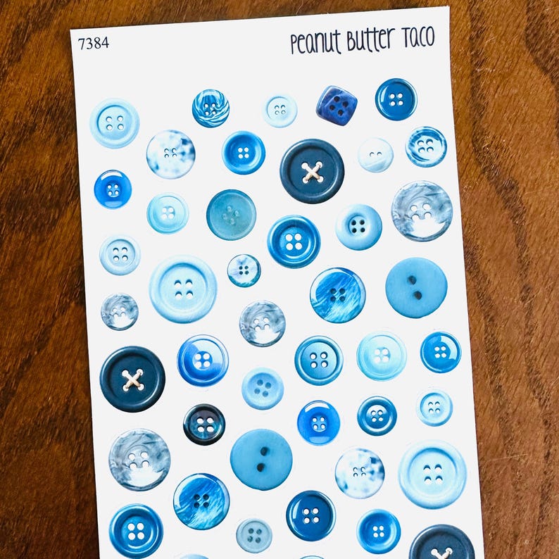 May include: A sheet of stickers featuring various blue buttons. The buttons vary in size, shape, and design, including some with marbled effects and X-shaped centers. The text "Peanut Butter Taco" is at the top.