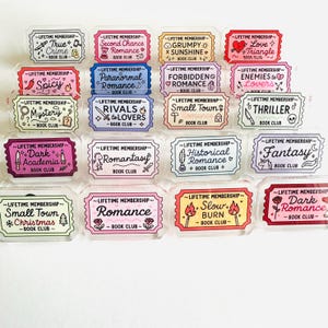 May include: A collection of twenty rectangular acrylic pins shaped like tickets, each featuring the text 'LIFETIME MEMBERSHIP' and a specific book club genre such as True Crime, Romance, Fantasy, or Thriller, decorated with colorful icons and illustrations.