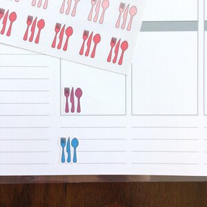 May include: A sheet of stickers with images of forks, knives, and spoons in pink, red, and blue. The stickers are arranged in rows and columns on a white background.