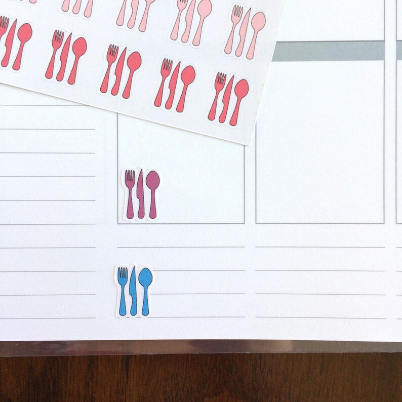 May include: A sheet of stickers with images of forks, knives, and spoons in pink, red, and blue. The stickers are arranged in rows and columns on a white background.