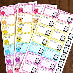 May include: Sheets of colorful planner stickers with the words "started" and "finished". The stickers feature illustrations of books, headphones, and e-readers. The stickers have a white background with various colored borders and patterns.