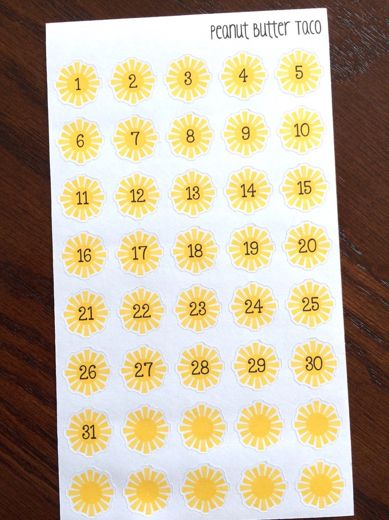 May include: Sheet of stickers with a yellow sunburst design and numbers 1-31. The text "Peanut Butter Taco" is printed at the top. The stickers are arranged in a grid pattern on a white background.