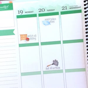 May include: A weekly planner with a green and white design. The planner has a list of chores for each day of the week. The chores include "switch out clothing", "wash/replace pillows", and "dust all surfaces".