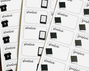 May include: Three sheets of white rectangular planner stickers with dashed borders. The stickers feature the text "started:" or "finished:" alongside black and white illustrations of e-readers, headphones, or closed books for tracking reading progress.