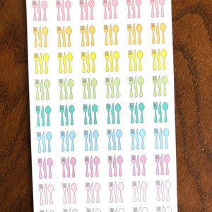 May include: A sheet of stickers with a variety of colored cutlery designs. The stickers are arranged in rows and columns, with each row featuring a different color. The colors include pink, yellow, green, blue, light pink, and gray. The text "Peanut Butter Taco" is printed at the top of the sheet.