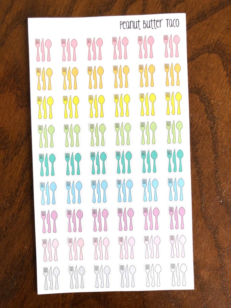 May include: A sheet of stickers with a variety of colored cutlery designs. The stickers are arranged in rows and columns, with each row featuring a different color. The colors include pink, yellow, green, blue, light pink, and gray. The text "Peanut Butter Taco" is printed at the top of the sheet.