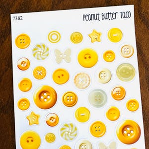 May include: A sheet of stickers featuring various yellow and cream-colored buttons in different sizes and shapes, including stars, butterflies, and swirl designs. The text "Peanut Butter Taco" is at the top.