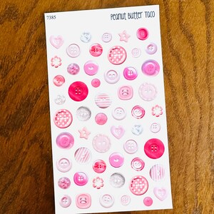 May include: A sheet of stickers featuring various pink and white buttons in different sizes and shapes, including hearts, stars, and flowers. The text "Peanut Butter Taco" is at the top.