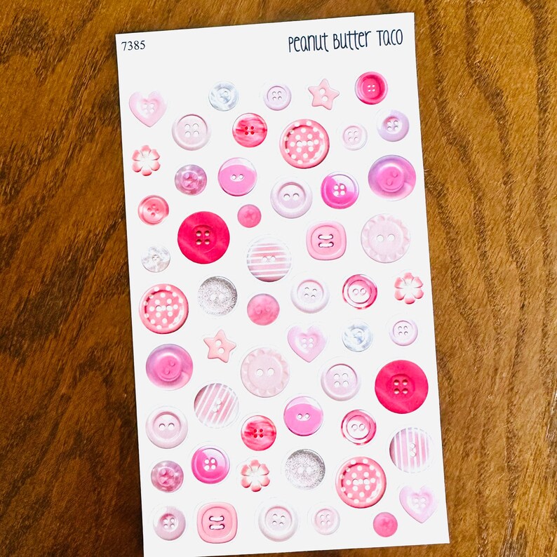 May include: A sheet of stickers featuring various pink and white buttons in different sizes and shapes, including hearts, stars, and flowers. The text "Peanut Butter Taco" is at the top.