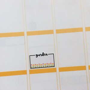 May include: A white sticker with a black border and the word "garden" written in black cursive. The sticker has a row of small pink, yellow, and green flowers along the bottom.