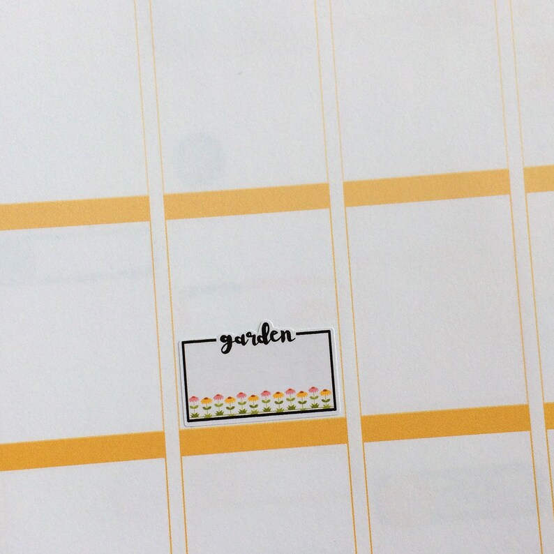 May include: A white sticker with a black border and the word "garden" written in black cursive. The sticker has a row of small pink, yellow, and green flowers along the bottom.