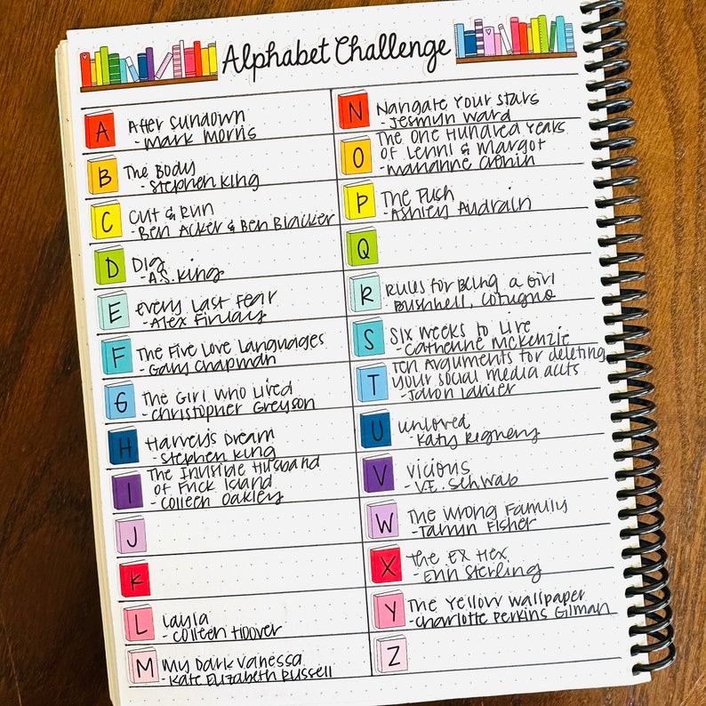 May include: A white notebook with a black spiral binding. The notebook has a list of books with their authors, organized alphabetically. The list is titled "Alphabet Challenge".
