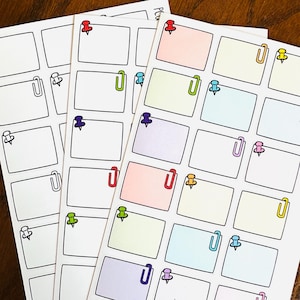 Peut inclure: Feuilles d'autocollants pour planificateur avec des boîtes rectangulaires, des trombones et des punaises de différentes couleurs. Les autocollants ont un fond blanc avec des contours noirs. Les punaises sont rouges, vertes, violettes et jaunes.