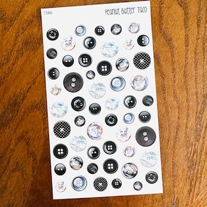 May include: A sheet of decorative buttons in various sizes and styles. The buttons are primarily black, gray, and white, with some featuring patterned designs. The text "Peanut Butter Taco" is at the top.