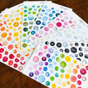 以下が含まれることがあります： さまざまなカラフルなボタンのデザインが施されたステッカーシートのコレクション。ステッカーは、赤、オレンジ、黄色、緑、青、紫など、さまざまな色を示しています。光沢のある仕上がりのステッカーもあれば、マットな仕上がりのステッカーもあります。