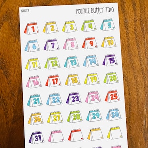 May include: A sheet of colorful calendar stickers with numbers 1 through 31. The stickers are shaped like small calendars with a heart at the bottom of each. The stickers are on a white background with the text "Peanut Butter Taco" and "8083" at the top.