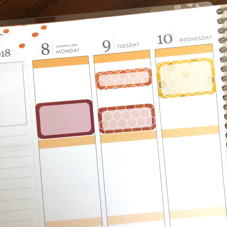 May include: A weekly planner with three columns labeled "Monday", "Tuesday", and "Wednesday". The dates "8", "9", and "10" are written above the columns. The planner has several decorative stickers with a honeycomb pattern in shades of brown, orange, and yellow.