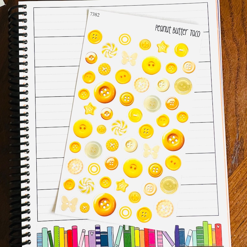 May include: A sheet of yellow and cream-colored buttons in various sizes and shapes, including stars, butterflies, and swirls. The sheet is labeled "Peanut Butter Taco" and "7382". The buttons are arranged on a lined notebook page.