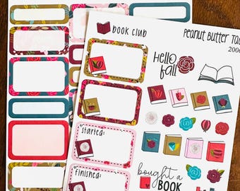 May include: Two sheets of adhesive planner stickers featuring a book club theme. The stickers include rectangular labels with floral and book motifs, text reading "book club," "hello fall," "started," "finished," and "bought a BOOK," plus various book and flower icons.
