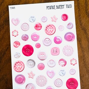 May include: A sheet of pink buttons in various shades and styles. The buttons include round, heart, and star shapes, with some featuring polka dots or stripes. The text "Peanut Butter Taco" is at the top right.