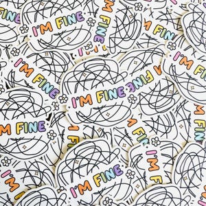 May include: White stickers with the text "I'M FINE" in a rainbow gradient font. Each sticker has a black scribble design and small flower and star illustrations. A collection of stickers.