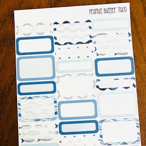 May include: A sheet of planner stickers with a nautical theme. The stickers feature rectangular and decorative shapes in shades of blue and white, with fish and wave patterns. The text "Peanut Butter Taco" is at the top.