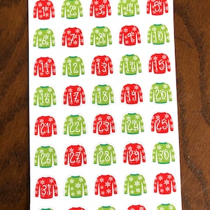 May include: Thirty-one Christmas-themed stickers featuring a red and green sweater design with snowflakes. The stickers are numbered 1 through 31. The text "Peanut Butter Taco" is at the top of the sheet.