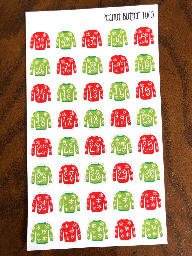 May include: Thirty-one Christmas-themed stickers featuring a red and green sweater design with snowflakes. The stickers are numbered 1 through 31. The text "Peanut Butter Taco" is at the top of the sheet.