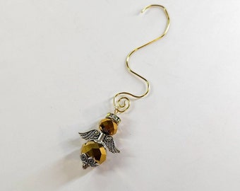 Op de afbeelding: Een handgemaakt engelenornament met een goudkleurige draadhaak. De engel heeft facetgeslepen amberkleurige kralen voor het lichaam en hoofd, met zilverkleurige metalen vleugels en decoratieve accenten. Een unieke kerstversiering.