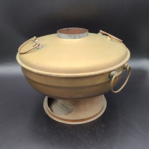 May include: A brass hot pot with two handles and a removable lid. The pot has a round base and is designed for cooking over a heat source.