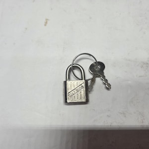 May include: A small, silver padlock with a key ring and two keys. The padlock has the word "WALSCO" printed on the front. The keys are attached to the ring. The items are on a white surface.