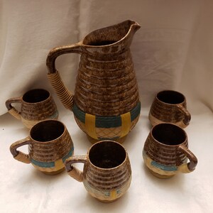 Puede incluir: Un juego de seis tazas de cerámica marrón y una jarra con un patrón tejido. Las tazas y la jarra tienen un diseño marrón, azul y amarillo.