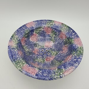 May include: A blue, green, and pink ceramic colander with a speckled pattern. The colander has a round shape and a small rim.
