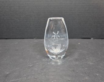 May include: Clear glass bud vase with an etched floral design. The vase has a rounded body and a narrow opening. The etched design features a flower with multiple petals and leaves. The vase is made of glass.