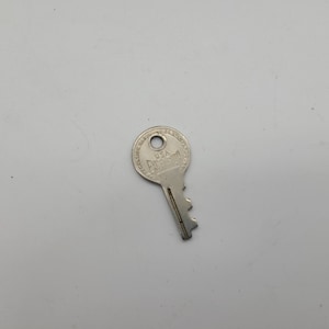 May include: A silver key with a round head. The head of the key has the text "USA  PARAGON" engraved on it.