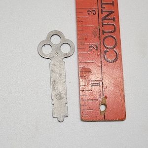 Könnte beinhalten: Ein silberfarbener Skelettschlüssel mit einem kleeblattartigen Kopf und der Nummer "2" auf dem Schaft. Der Schlüssel ist etwa 5 cm lang und wird neben einem Lineal gezeigt.