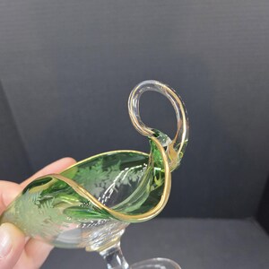 Op de afbeelding: Een groene en heldere glazen serveerschaal met een gouden rand en handvat. De schaal heeft een decoratief ge&euml;tst bloemmotief. Het handvat is van helder glas met gouden accenten.