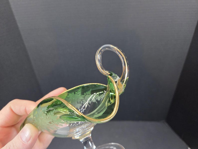 Op de afbeelding: Een groene en heldere glazen serveerschaal met een gouden rand en handvat. De schaal heeft een decoratief ge&euml;tst bloemmotief. Het handvat is van helder glas met gouden accenten.