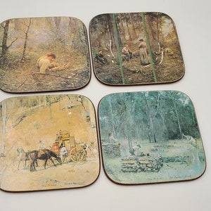 May include: Set of four square coasters featuring images of people and landscapes in a woodland setting. The coasters are made from cork and have a brown wooden frame.