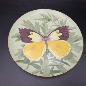May include: A decorative ceramic plate with a yellow and purple butterfly on a green leafy background.